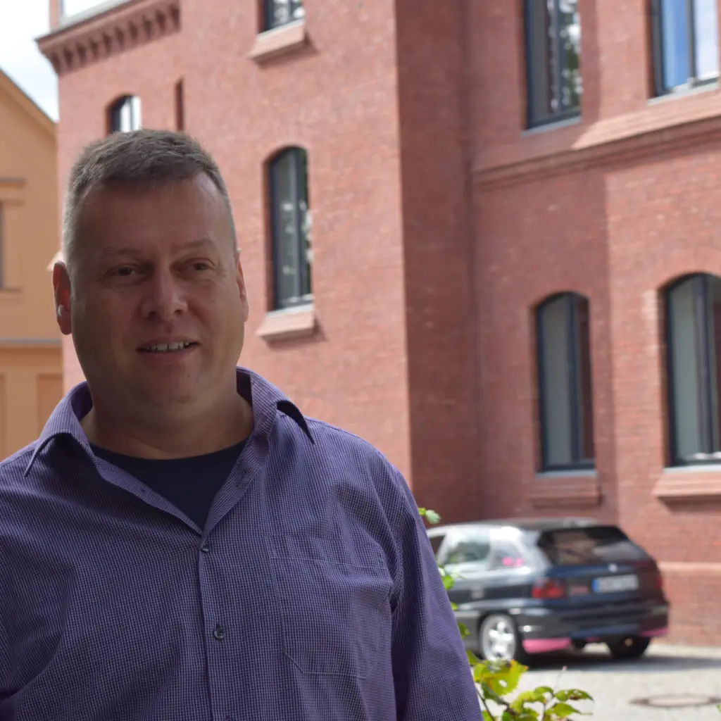 Stadtverordneter Uwe Fröhlich (Bündnis 90/ Die Grünen) steht vor einem roten Backsteingebäude und berichtet über Fairtrade-Towns. Foto: Lilith Grull