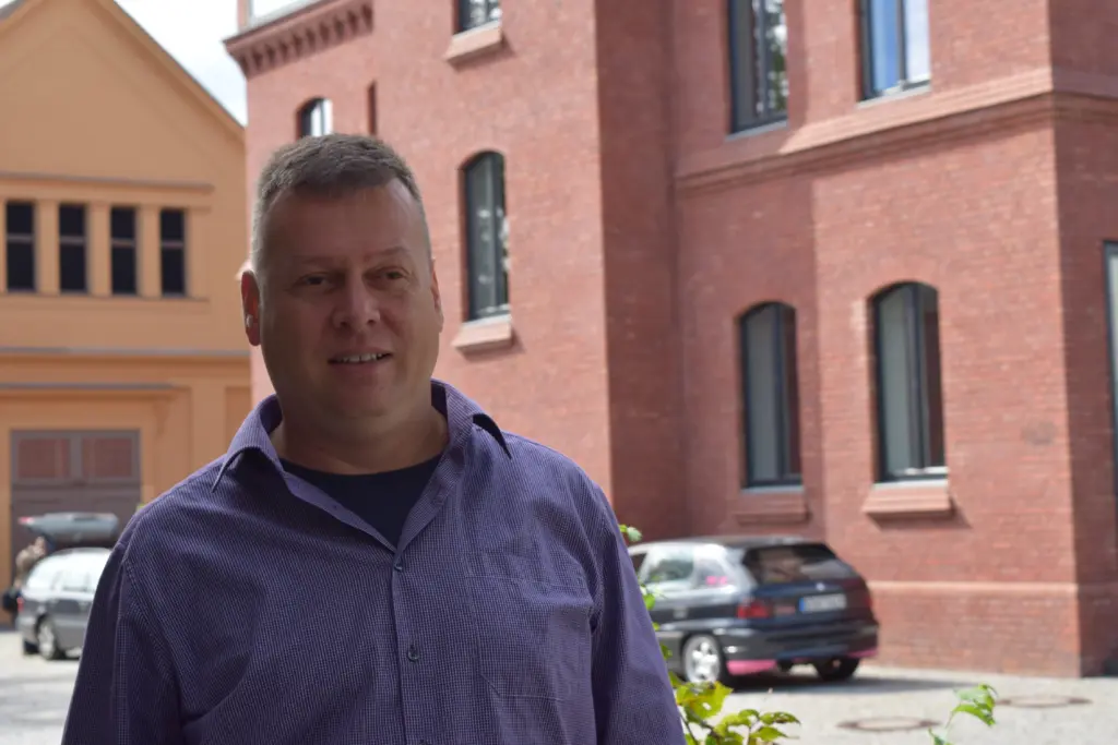 Stadtverordneter Uwe Fröhlich (Bündnis 90/ Die Grünen) steht vor einem roten Backsteingebäude und berichtet über Fairtrade-Towns. Foto: Lilith Grull