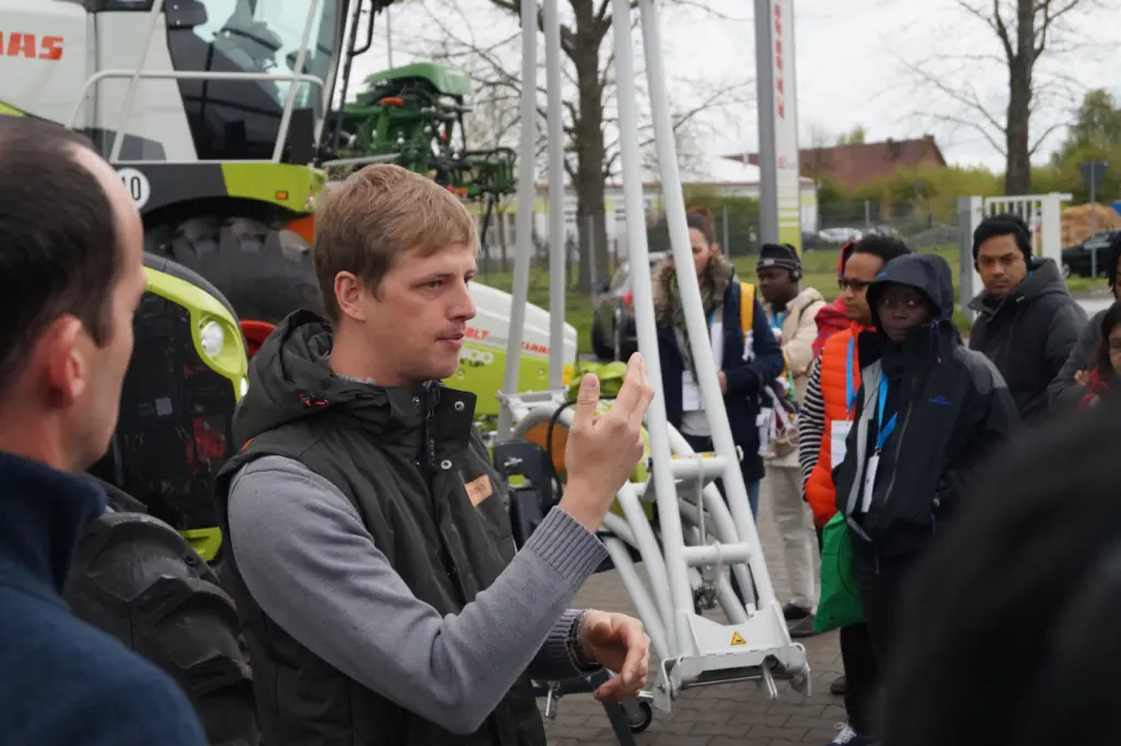 'CLAAS' Mitarbeiter Malzahn erklärt der internationalen Gruppe einen Mähdrescher