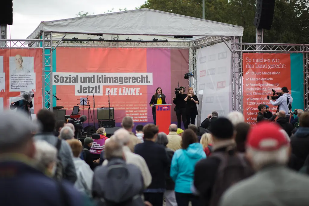Die Bühne der Partei "Die Linke" bei deren Kundgebung am Neptunbrunnen. Auf der Bühne steht die Parteivorsitzende Janine Wissler, im Vordergrund stehen einige Menschen die ihr zuhören.