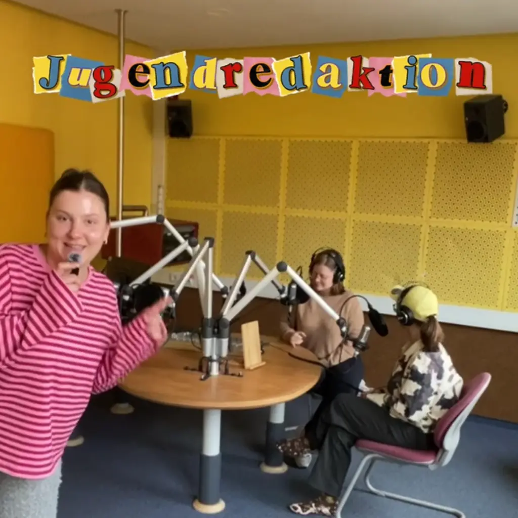 Teilnehmer*innen sitzen im Hintergrund an einem Radiotisch. Im Vordergrund Spricht eine Person in ein kleines Mikro. Über der Szene steht in bunten Buchstaben "Jugendredaktion".