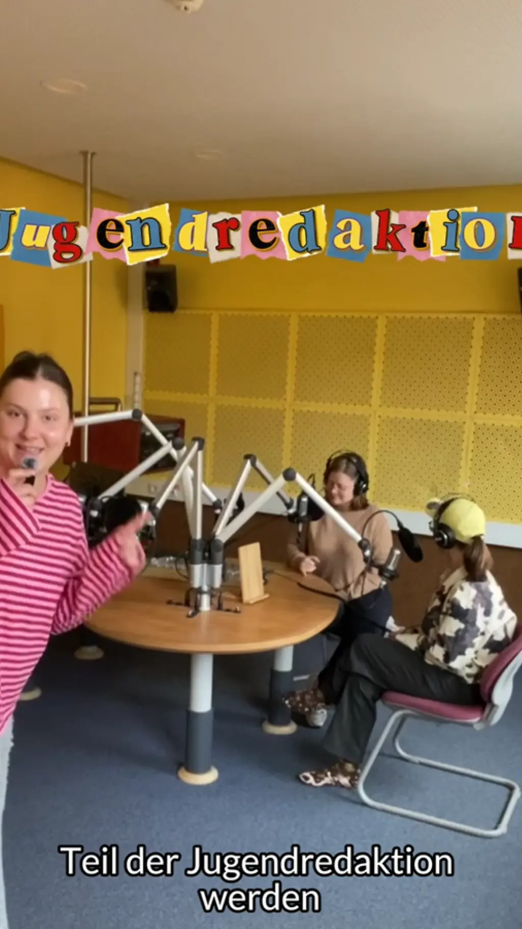Teilnehmer*innen sitzen im Hintergrund an einem Radiotisch. Im Vordergrund Spricht eine Person in ein kleines Mikro. Über der Szene steht in bunten Buchstaben "Jugendredaktion".